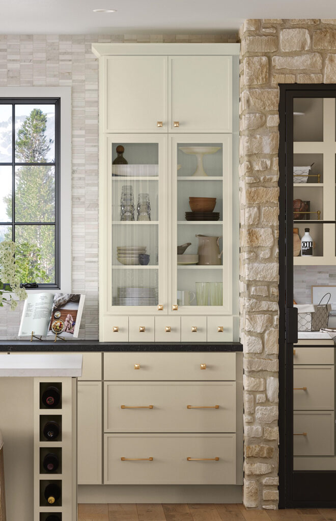 Cream kitchen cabinets with a glass-front display, set next to a stone-clad wall.