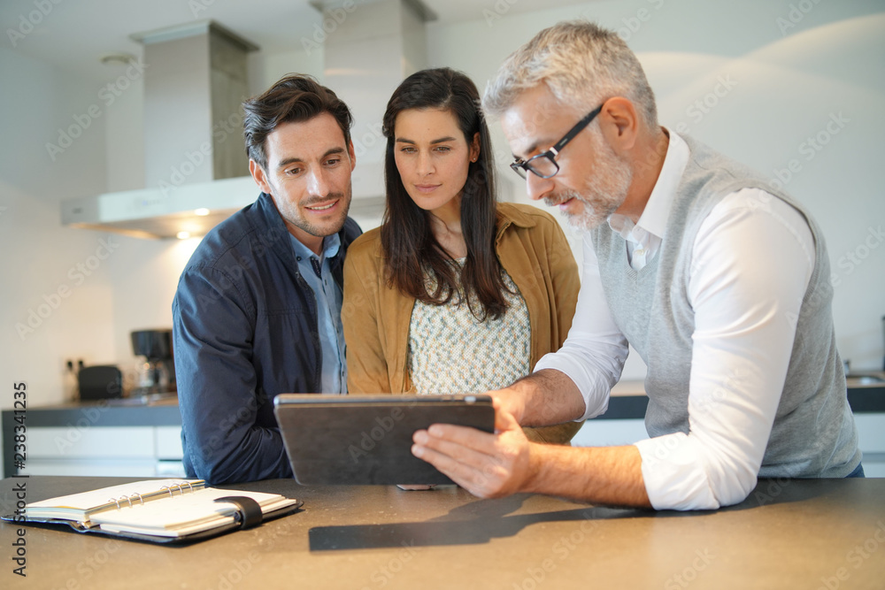 A man conducting a cabinet design consultation with a couple in a kitchen.