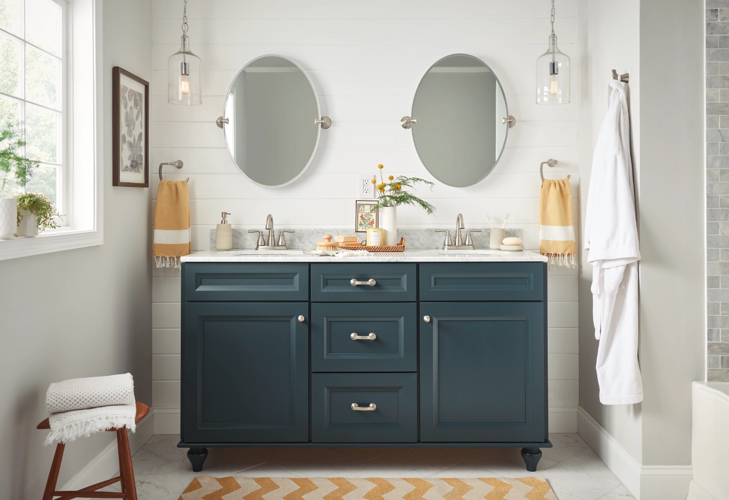 Blue bathroom cabinets with a marble countertop, double vanity, and two oval mirrors.