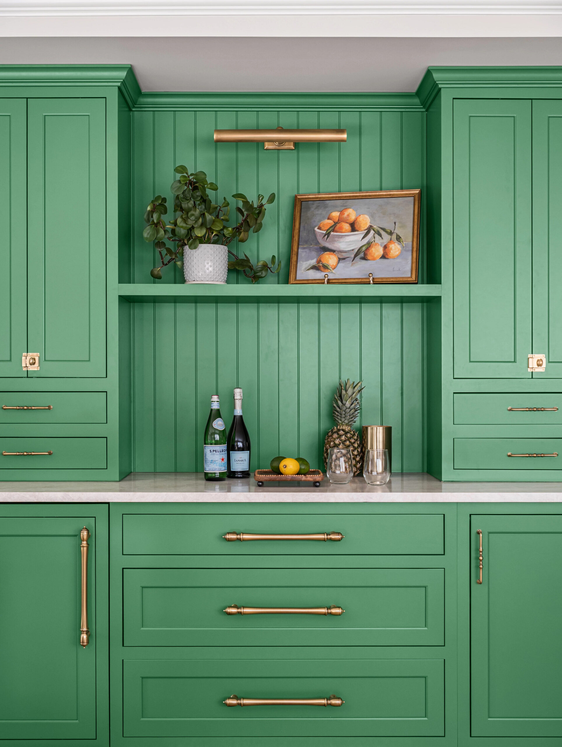 Green kitchen cabinets with a central shelf for a cabinet design consultation, plants, and art.