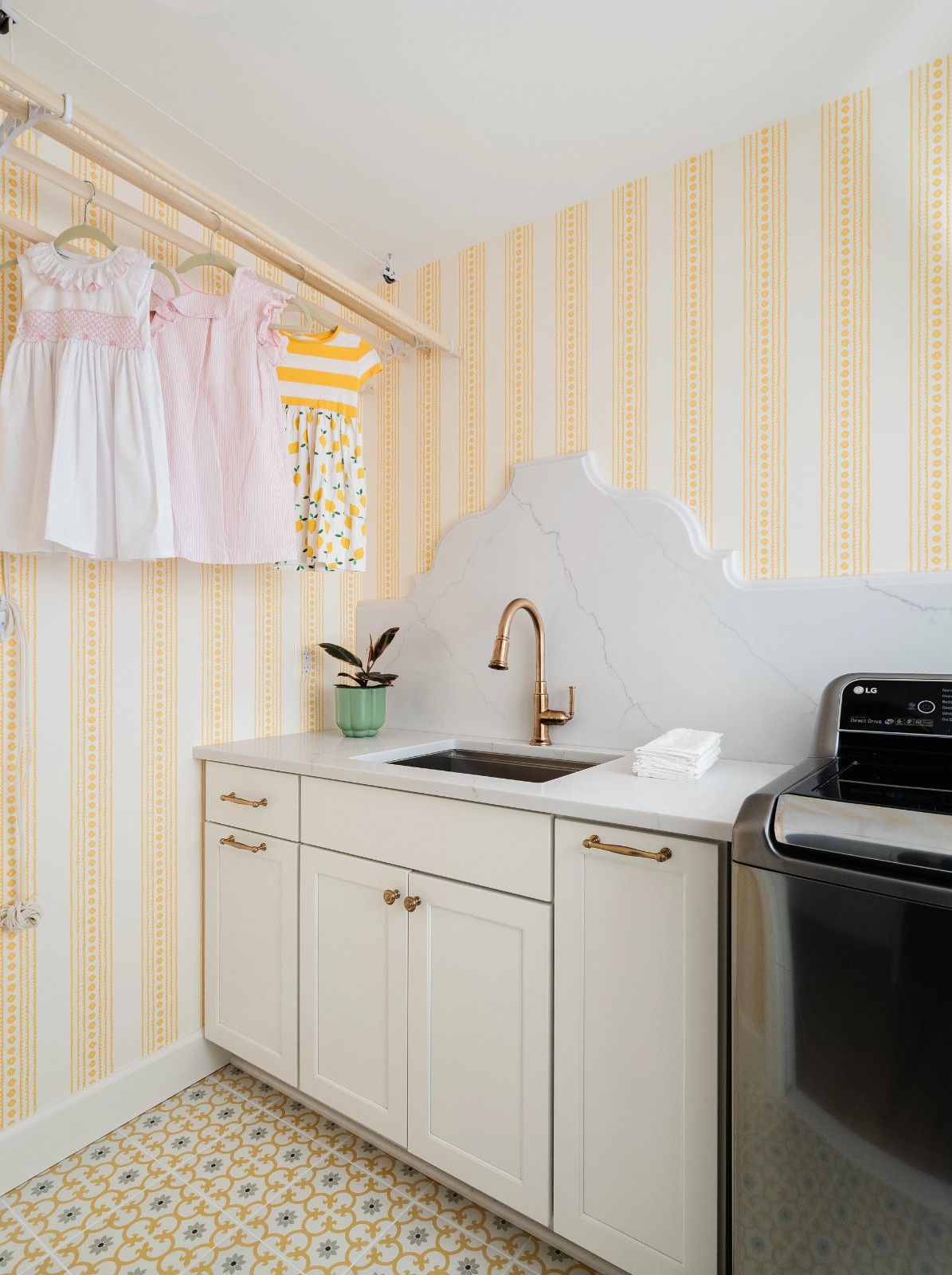Laundry room with yellow striped wallpaper, a white sink, and baby dresses for cabinet design.