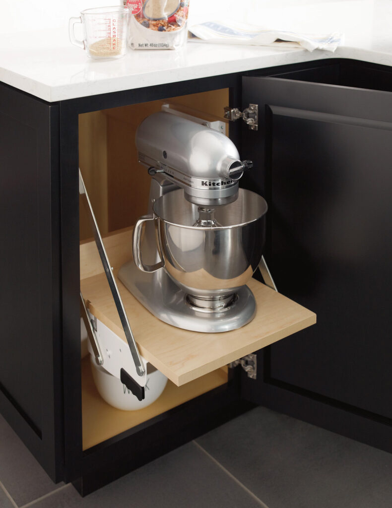A silver stand mixer on a pull-out shelf inside a kitchen cabinet.