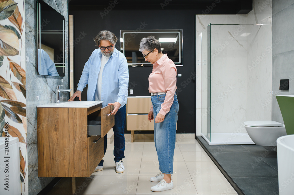 A man and woman standing in a bathroom showroom looking at wooden bathroom cabinets.