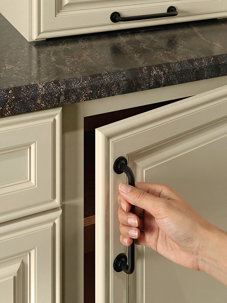 A hand pulls open a cream-colored kitchen cabinet door with a black handle.