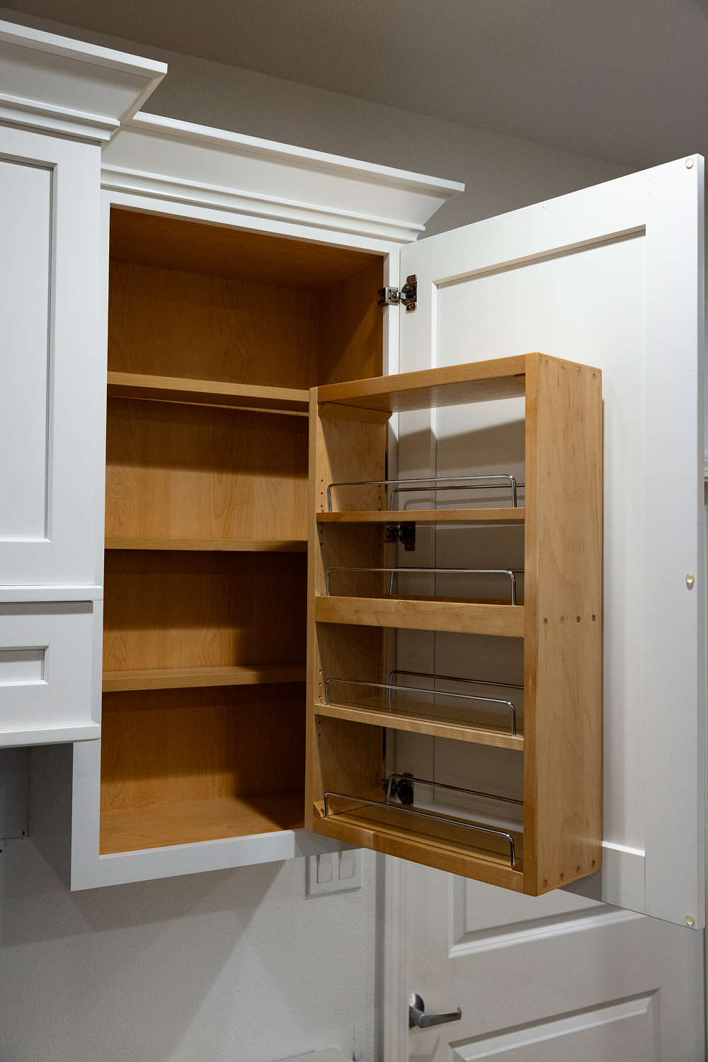 White upper kitchen cabinet display featuring a pull-out door spice rack and shelf organizer at the Bay Area Cabinet Supply showroom in the Bay Area.
