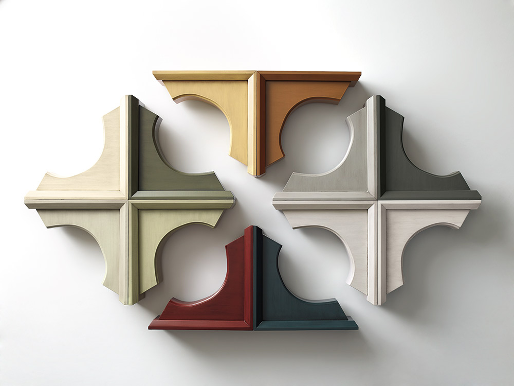 Eight wooden corbels for kitchen cabinets arranged in a cross pattern on a white wall.